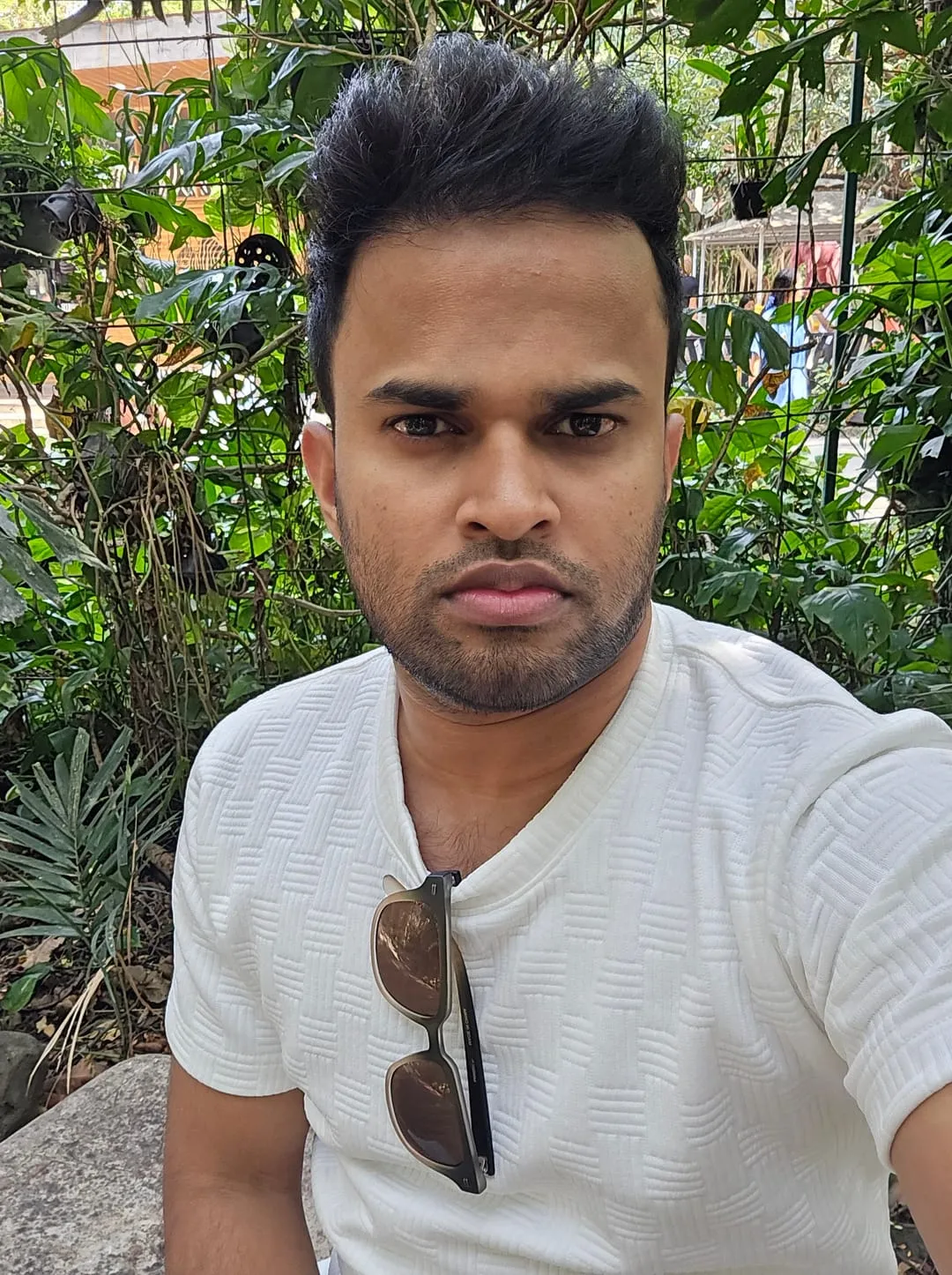 Abhith Rajan in a white textured T-shirt with sunglasses hooked on the collar, taking a selfie in a leafy garden